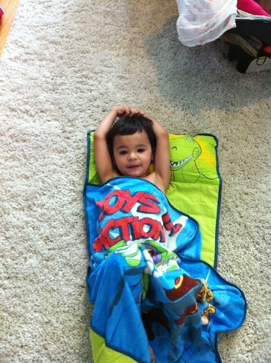 A preschooler who needs more sleep, wrapped in a blanket lying on its back on the floor