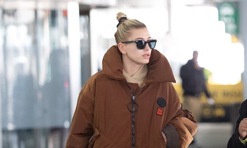 Hailey Baldwin on the airport with a sleek bun hairstyle and puffer brown jacket. 