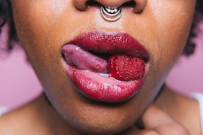 A woman holding a raspberry with her mouth
