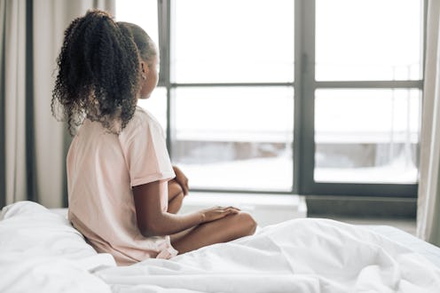 A small girl with endometriosis sitting on her bed and looking through the window