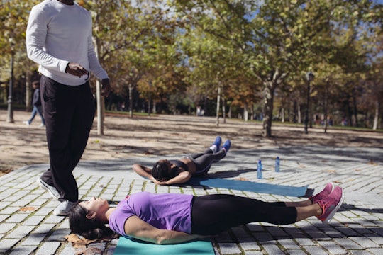 Two women with pelvic floor disorder on yoga mats exercising outside with their coach.