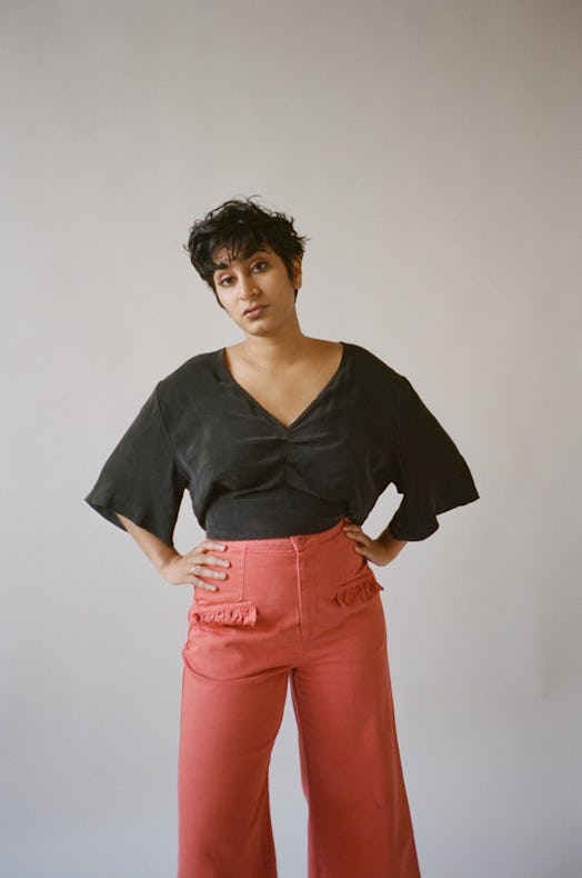 Poet Fatimah Asghar with a short haircut wearing a black top and pink pants while posing