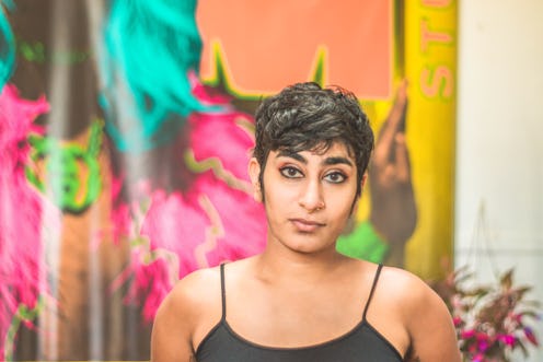 Poet Fatimah Asghar with a short haircut, wearing a black tank top in front of a colorful graffiti w...