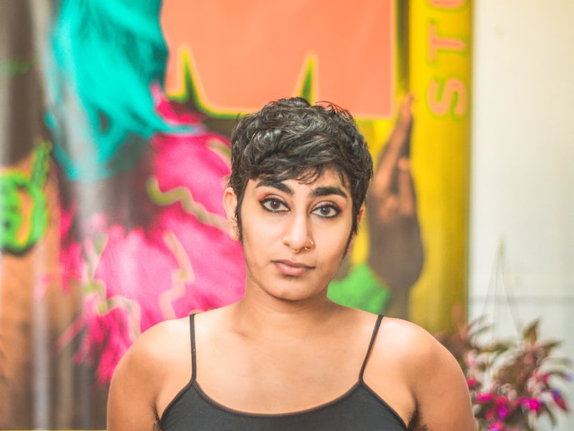 Poet Fatimah Asghar with a short haircut, wearing a black tank top in front of a colorful graffiti w...