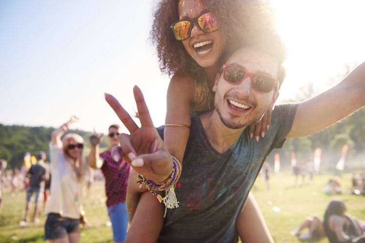 A guy gives his girlfriend a piggyback ride while she makes a peace sign at a festival.