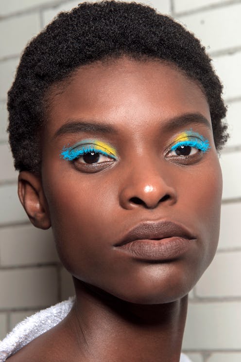 A model with short hair and dark skin, wearing bright eyeshadow in blue and yellow
