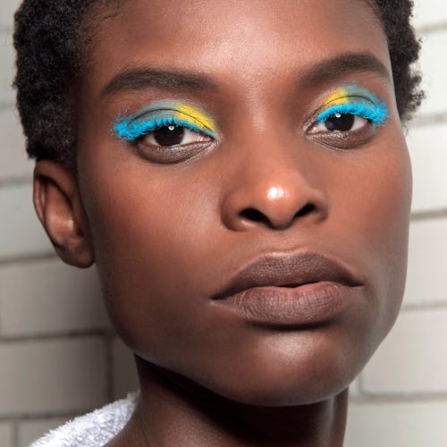 A model with short hair and dark skin, wearing bright eyeshadow in blue and yellow