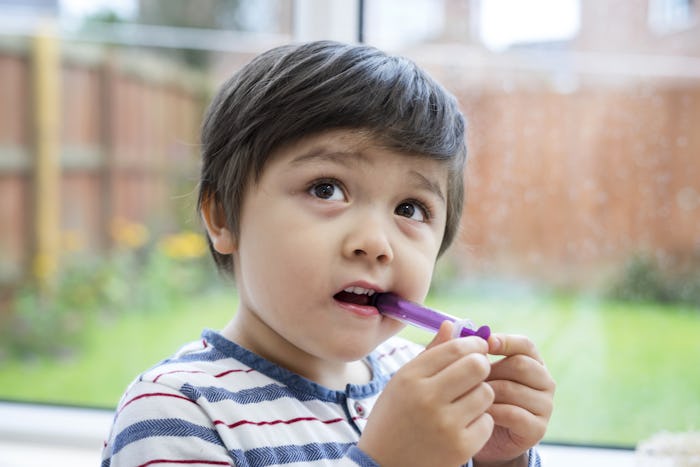A toddler boy holding a purple Tylenol syringe in his mouth