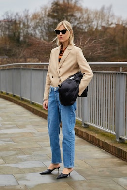 Young blonde lady posing in a light brown blazer jacket, jeans, and blue heels