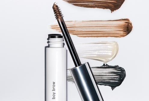 A tube of Glossier's Boy Brow with its different shades smudged in the background