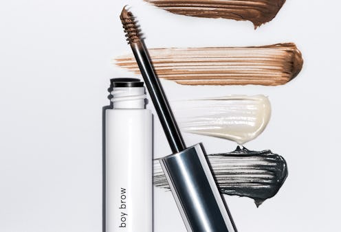 A tube of Glossier's Boy Brow with its different shades smudged in the background 