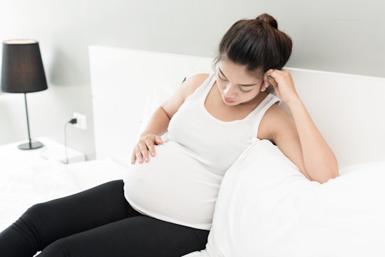 A pregnant woman sitting on her bed, with her hand on her stomach