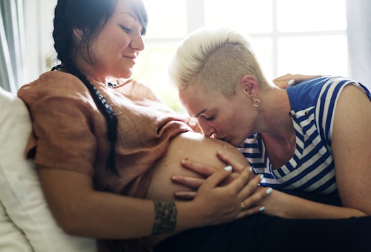An LGBTQ+ couple with one parent kissing the other's pregnant belly 