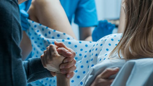 A laboring woman holding her partner's hand as she gives birth. 