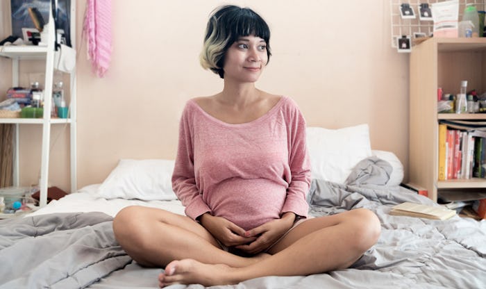 Pregnant woman in a pink shirt sitting cross-legged on her bed