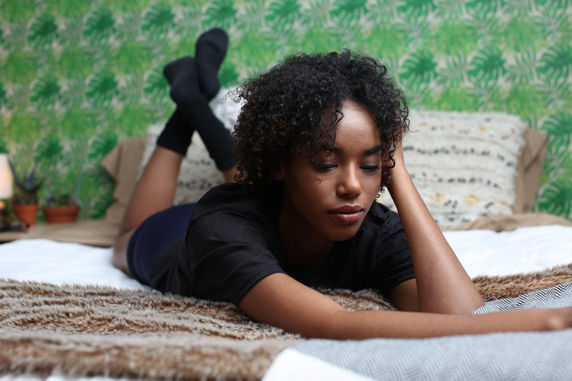 A young woman with short curly hair lying on her stomach on a bed with a green wallpaper in her back...