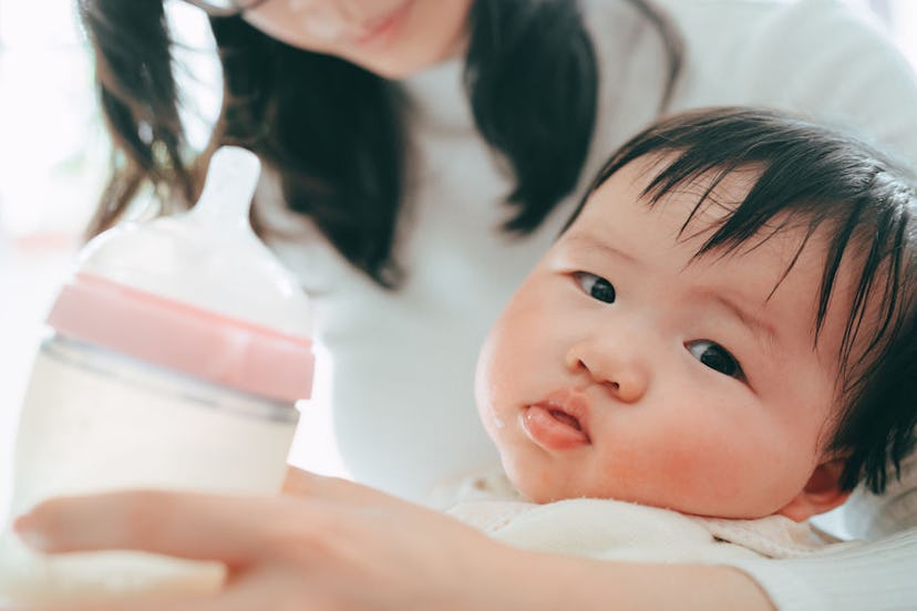 A mother holding her toddler and a bottle of synthetic breast milk