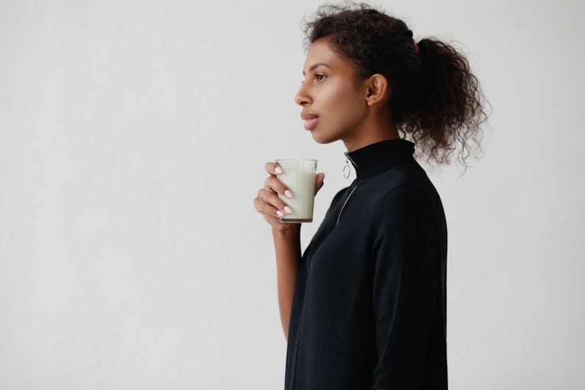 A woman with her curly hair in a ponytail, holding a glass of synthetic breast milk