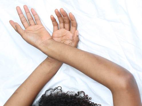 Arms of a woman on chemotherapy crossed on a white bed sheets.