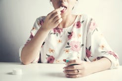A woman in a white shirt with a floral pattern sitting at a table and taking pills