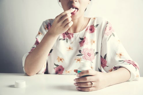 A woman in a white shirt with a floral pattern sitting at a table and taking pills