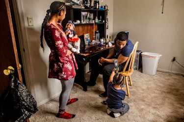 Ambreia Meadows-Fernandez standing in a home room with her baby, toddler, and husband Enrico