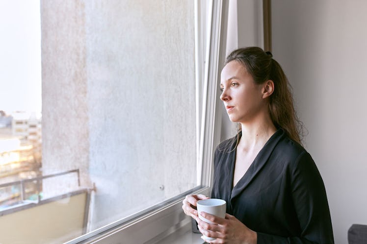 A girl with cold, looking through a window while holding a cup of tea.