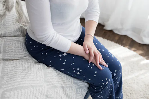 A woman with a depression gene sitting in her pajamas on the bed.