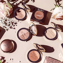 Too Faced bronzers in different shades next to roses and white flowers on the makeup desk