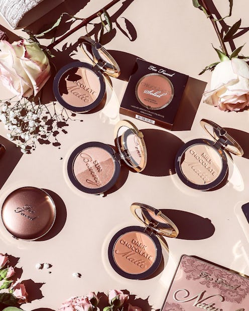 Too Faced bronzers in different shades next to roses and white flowers on the makeup desk