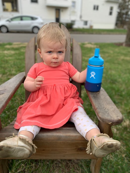 A baby sitting on a wooden chair with an angry facial expression