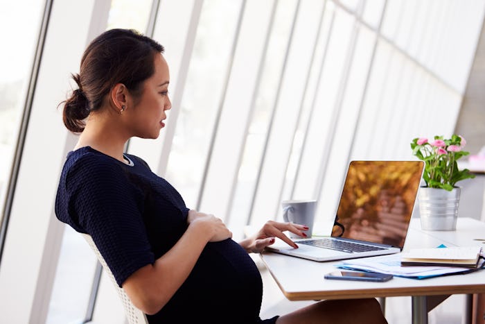 pregnant woman sitting at desk working on laptop