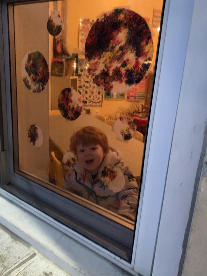 A little kid looking out of the daycare window excited for daycare pickup 