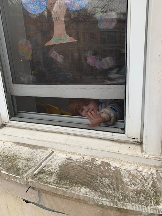 A child peaking out of the Daycare window, sticking its hand out 