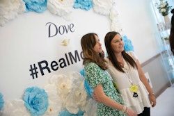 Two women posing in front of the banner at the The Dove Activations at Mom 2.0 event