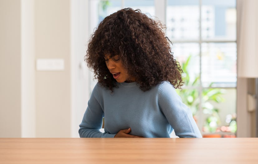 A curly and black-haired girl holding her stomach with her hands because of pain caused by IBS
