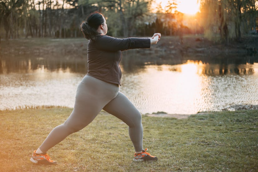 A woman in her gym clothes stretching out on a yoga mat next to a river