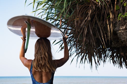 A woman holding a surfboard over her head while looking to a sea