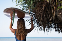 A woman holding a surfboard over her head while looking to a sea