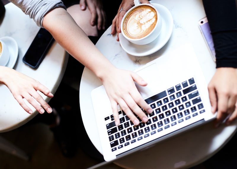 A man and a woman looking at a laptop standing on a table next to a cup of latte