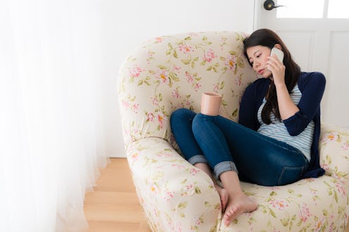 A woman on the floral-patterned sofa talking on the phone while holding a cup of coffee.