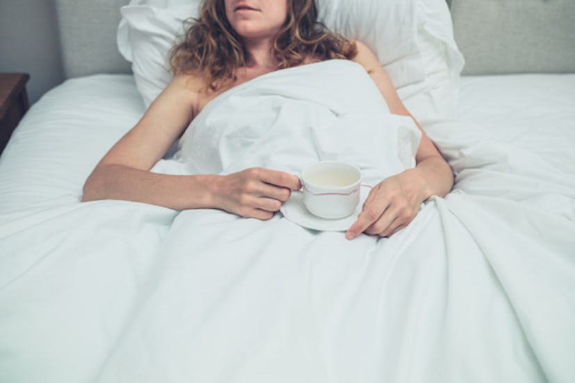  A woman lying in the bed in morning and holding a cup of coffee.