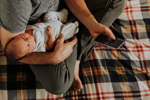 A father reading a Father's Day text while holding his first baby and sitting on tartan sheets