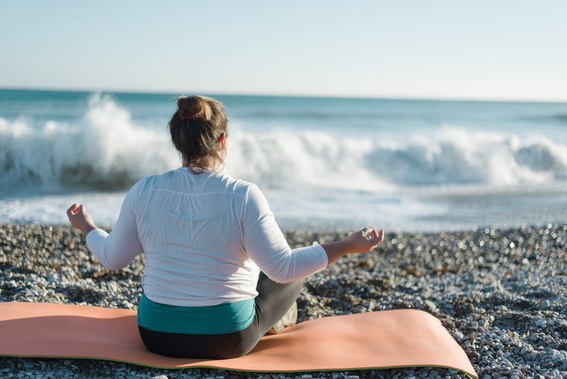 A woman meditating on her yoga mat with the sea in front of her