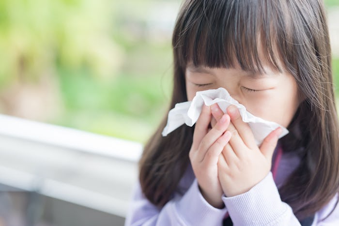 A little girl wiping her nose with a white napkin because she has indoor allergies