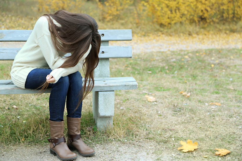 A woman in depression sitting on a park bench and crying while her hair is covering her face