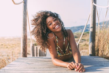 A happy woman in a tropical bikini lays down on the boardwalk leading to the beach on a sunny day.