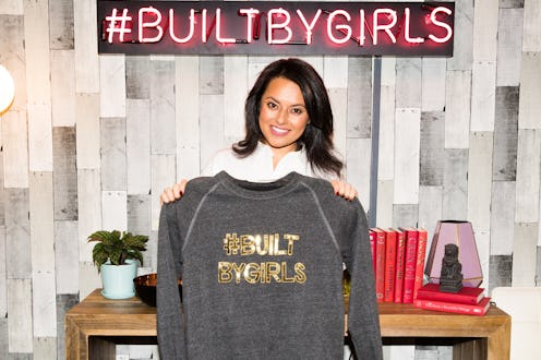 Nisha Dua, the founder of #BUILTBYGIRLS, holding a grey hoodie with her platform's name in gold