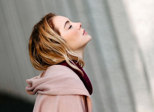 A blonde woman wearing a light pink hoodie, with her eyes closed, tilting her head back and looking ...