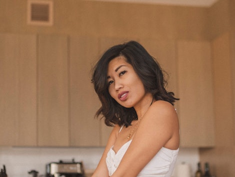Lisa Linh posing in a white top next to a couch on a kitchen